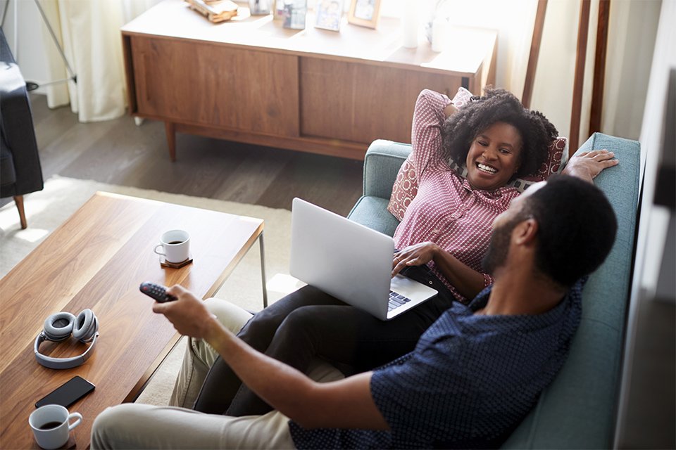 A couple with a laptop sitting on a sofa.